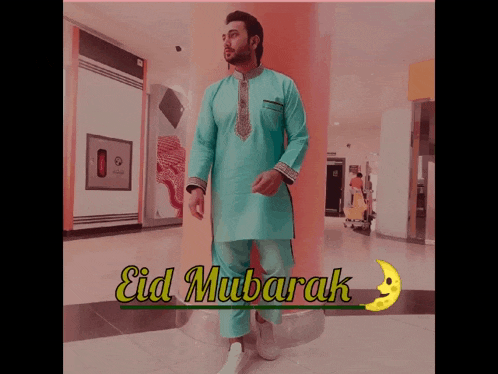 a man in a blue shirt and pants is standing in front of a sign that says eid mubarak