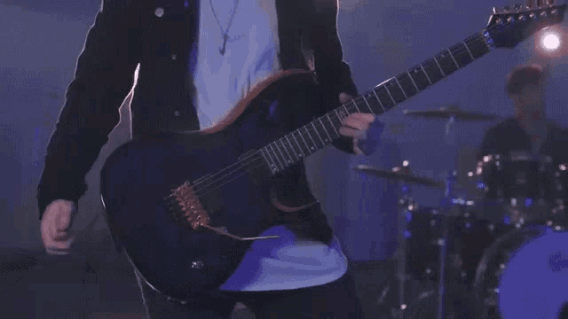 a man in a black jacket is playing a guitar on stage .