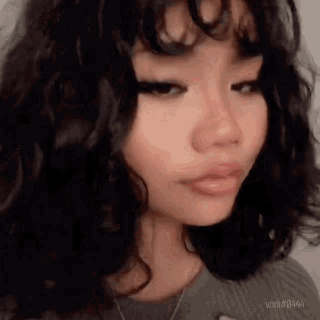 a close up of a girl with curly hair and a necklace .