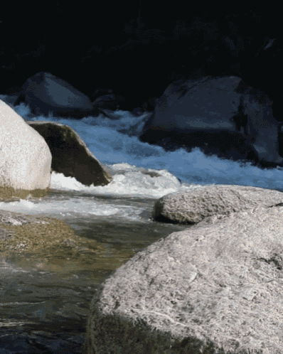 a river with rocks in the foreground and a large rock in the background