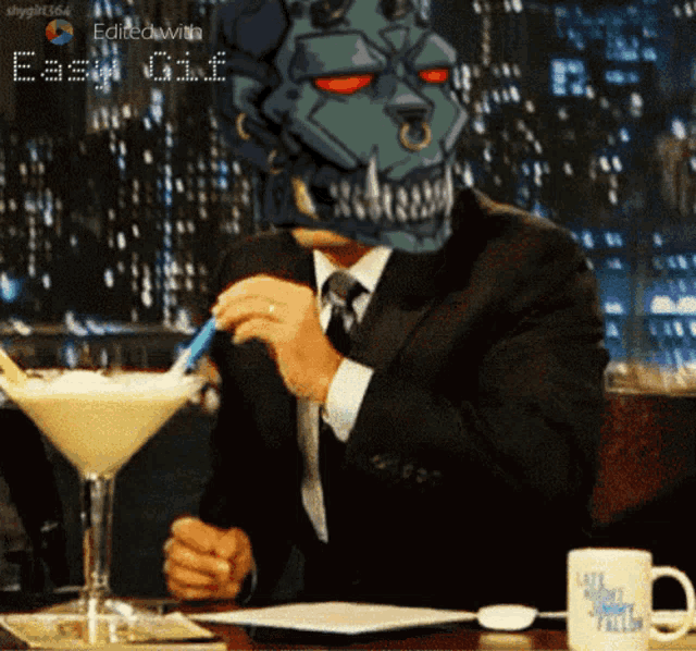 a man in a suit sits at a table with a martini glass and a mug that says late night talk
