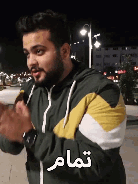 a man with a beard is wearing a green and yellow jacket with arabic writing on the sleeves