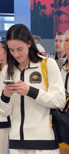 a woman wearing a white jacket with iowa on the front looks at her phone
