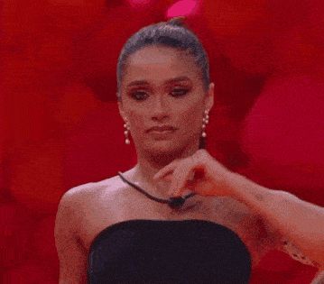 a woman in a black dress is holding her hair in a ponytail while standing in front of a red background .