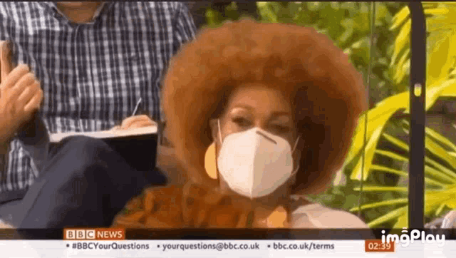 a woman with an afro is wearing a face mask on a television show .