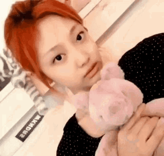 a woman with red hair is holding a pink teddy bear in her hands .