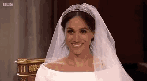 meghan markle is wearing a wedding dress and veil and smiling .