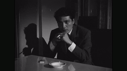 a man in a suit sits at a table with a cigarette in his hand