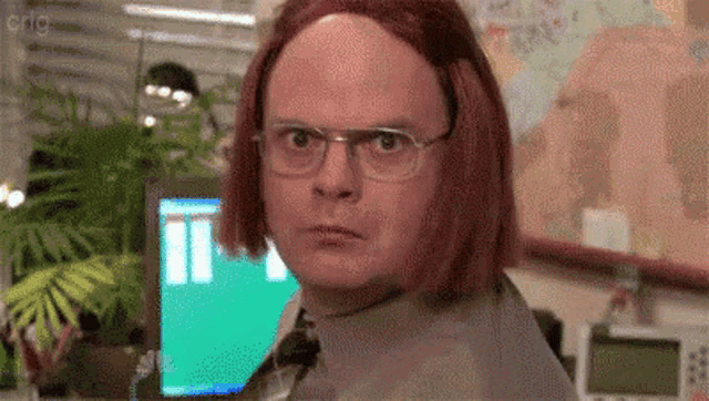 a man with red hair and glasses is sitting at a desk in front of a computer .