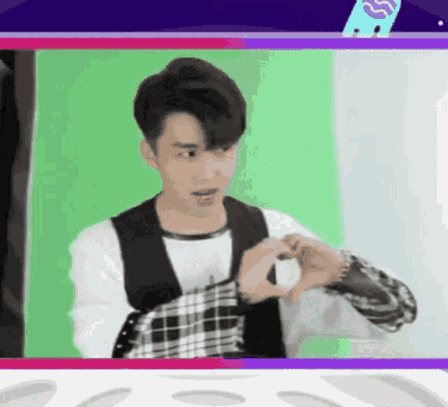 a man making a heart with his hands in front of a green screen