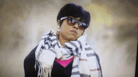 a woman wearing sunglasses and a scarf is standing in front of a camera .
