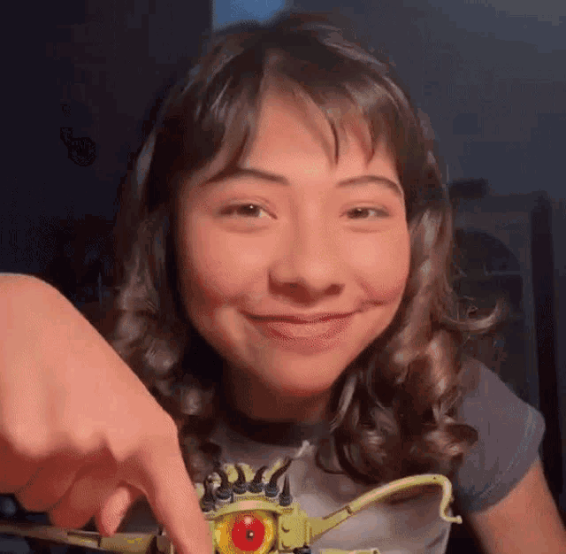 a young girl is smiling while pointing at a toy with a red eye .