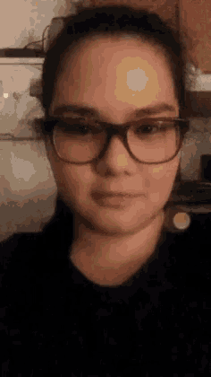 a woman wearing glasses and a black shirt is taking a selfie