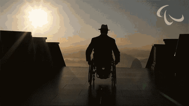 a silhouette of a man in a wheelchair with the sun shining behind him
