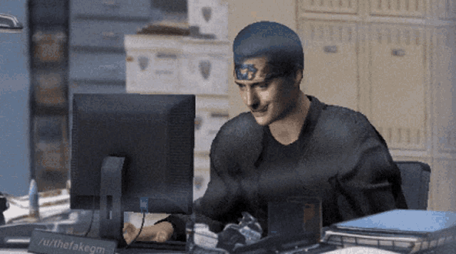 a man sits at a desk in front of a computer with a sign that says allthetakergm on it