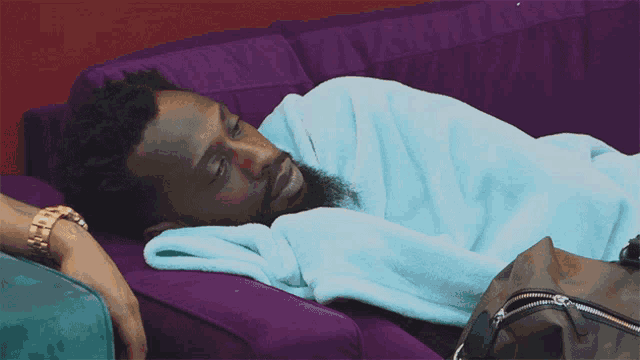 a man laying on a purple couch with a blue blanket on him