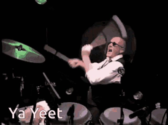 a man is playing drums on a stage in a dark room while a sausage is flying in the air .