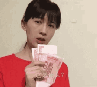 a woman in a red shirt is holding up a bunch of money .