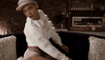 a man in a hat is sitting on a couch in underwear .
