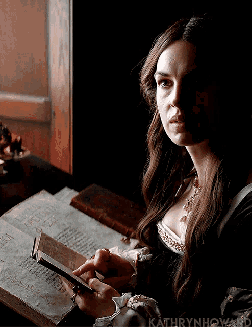 a woman sitting at a table reading a book with kathryn howard in the corner