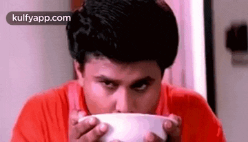 a man in a red shirt is eating out of a bowl .