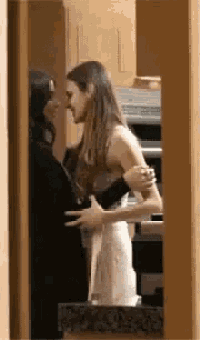 two women are standing next to each other in a kitchen and hugging .