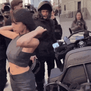 a woman in a crop top is standing next to a man in a helmet on a motorcycle