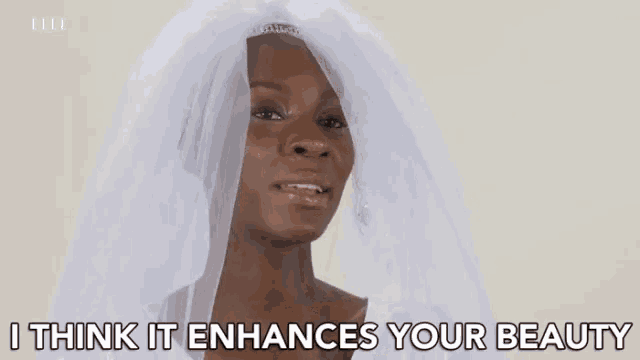 a woman in a wedding dress with a veil on her head says `` i think it enhances your beauty ''