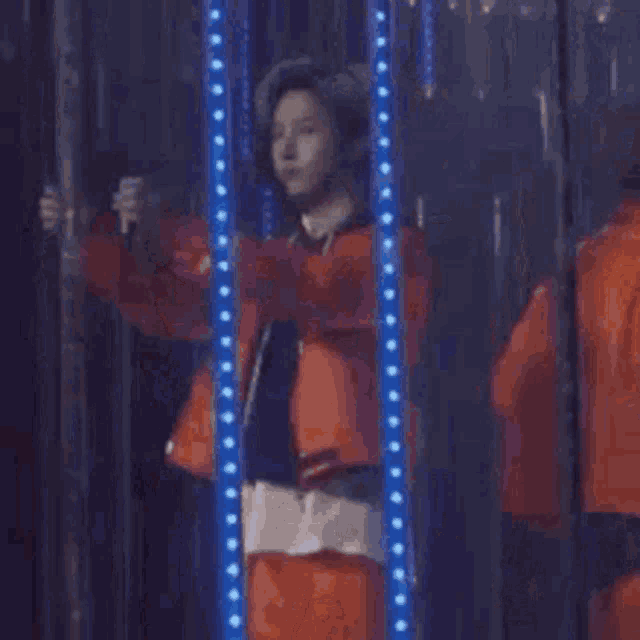 a person in an orange jacket is standing in front of a microphone in a dark room .