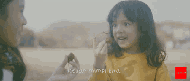 a little girl holding a piece of food with the words kejar mimpi kita written on the bottom