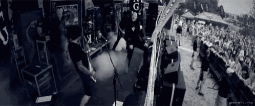 a man playing a guitar in front of a crowd with the letters g on the back of his shirt