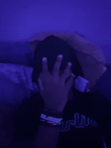 a person is covering their face with their hand in a dark room with purple lights .