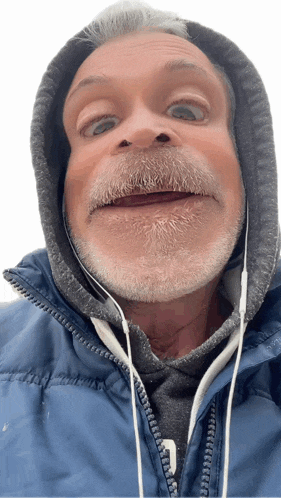 a man with a beard wearing a blue jacket and headphones making a funny face