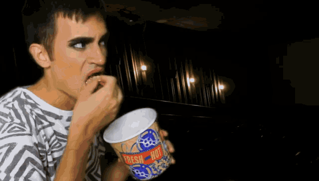 a man in a striped shirt is eating popcorn from a fresh hot bucket