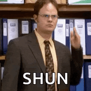 a man in a suit and tie is giving the middle finger in front of a shelf of folders .