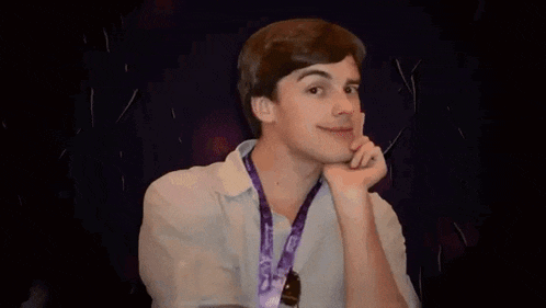 a young man with a purple lanyard around his neck is smiling and holding his hand to his chin .