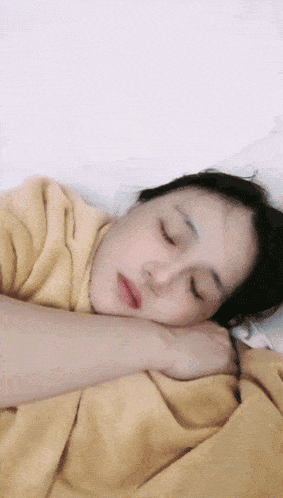 a woman laying in bed with her eyes closed and a yellow blanket