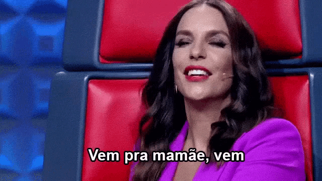 a woman in a purple jacket is sitting in a red chair and says vem pra mamae , vem .