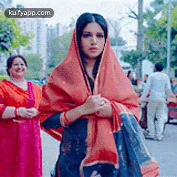 a woman wearing a scarf is walking down a street with other women .