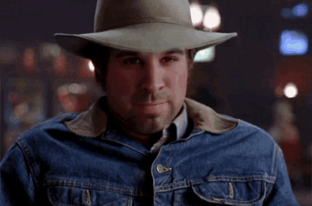a man wearing a cowboy hat and a denim jacket smiles for the camera