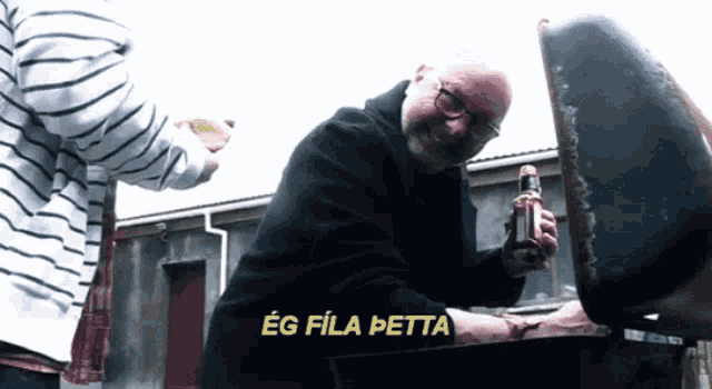 a man holding a bottle of beer in front of a grill that says eg fila petta on it