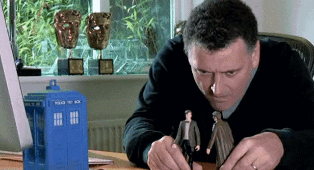 a man is sitting at a desk with a police box in the background