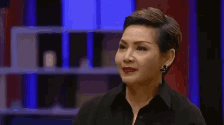 a woman with short hair is wearing a black shirt and earrings and making a funny face .