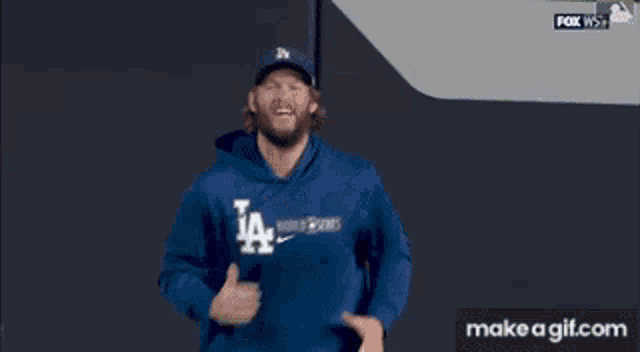 a man in a la dodgers sweatshirt is running on a baseball field .