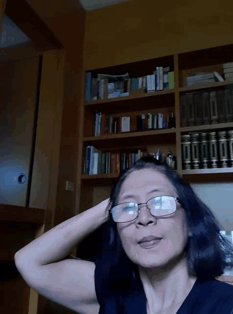 a woman wearing glasses is standing in front of a bookshelf with books on it