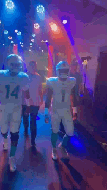 a group of football players are walking down a hallway with purple lights