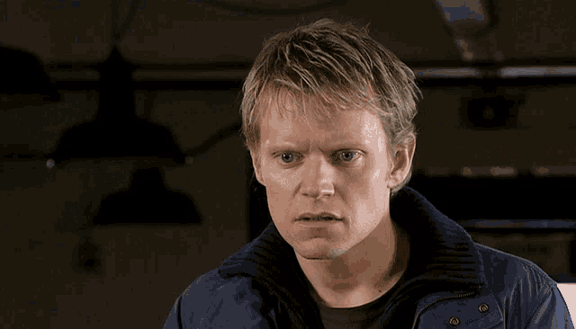 a man in a blue jacket looks at the camera with a serious look on his face