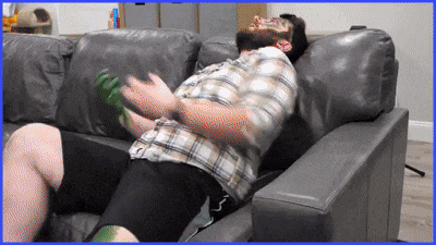 a man in a plaid shirt is laying on a couch with a green bottle in his hand