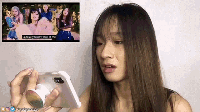 a woman is holding a cell phone in front of a screen that says look at you now look at me on it