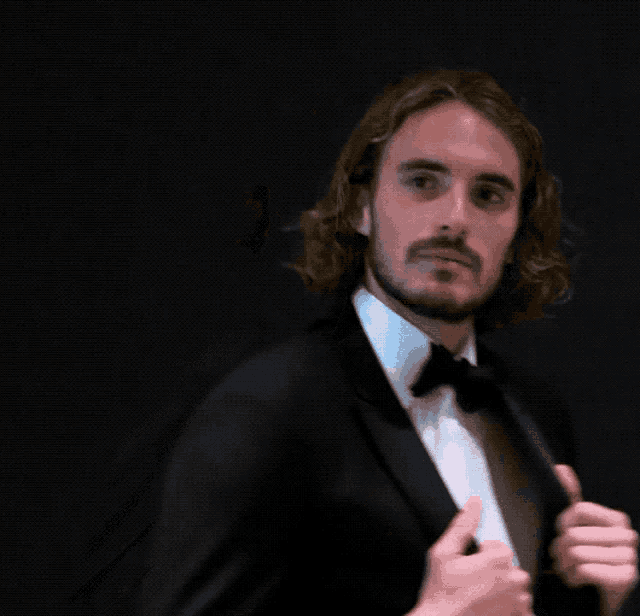 a man with long hair and a beard is wearing a suit and bow tie